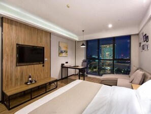 A modern hotel room with a large bed, a desk, a chair, a TV, and a city view through large windows. - GreenTree Eastern Yancheng Administration Center Hotel (Yancheng)