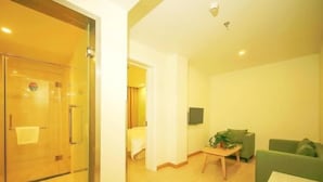 A hotel room with a glass door, a green sofa, a small table with a plant, and a TV mounted on the wall. - Shell Langfang GuAn County Bus Station Hotel (Langfang)