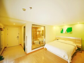 Une chambre d’hôtel comprenant un lit, une salle de bain avec une douche à parois de verre et une porte donnant sur une autre pièce.