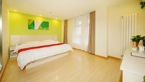 A modern hotel room with a large bed, a bedside table, a nightstand, a window with curtains, a radiator, and a small plant on the desk. - Shell Langfang GuAn County Bus Station Hotel (Langfang)
