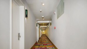 A hotel hallway with a colorful geometric patterned floor, white walls, and doors on either side. - Shell Langfang GuAn County Bus Station Hotel (Langfang)
