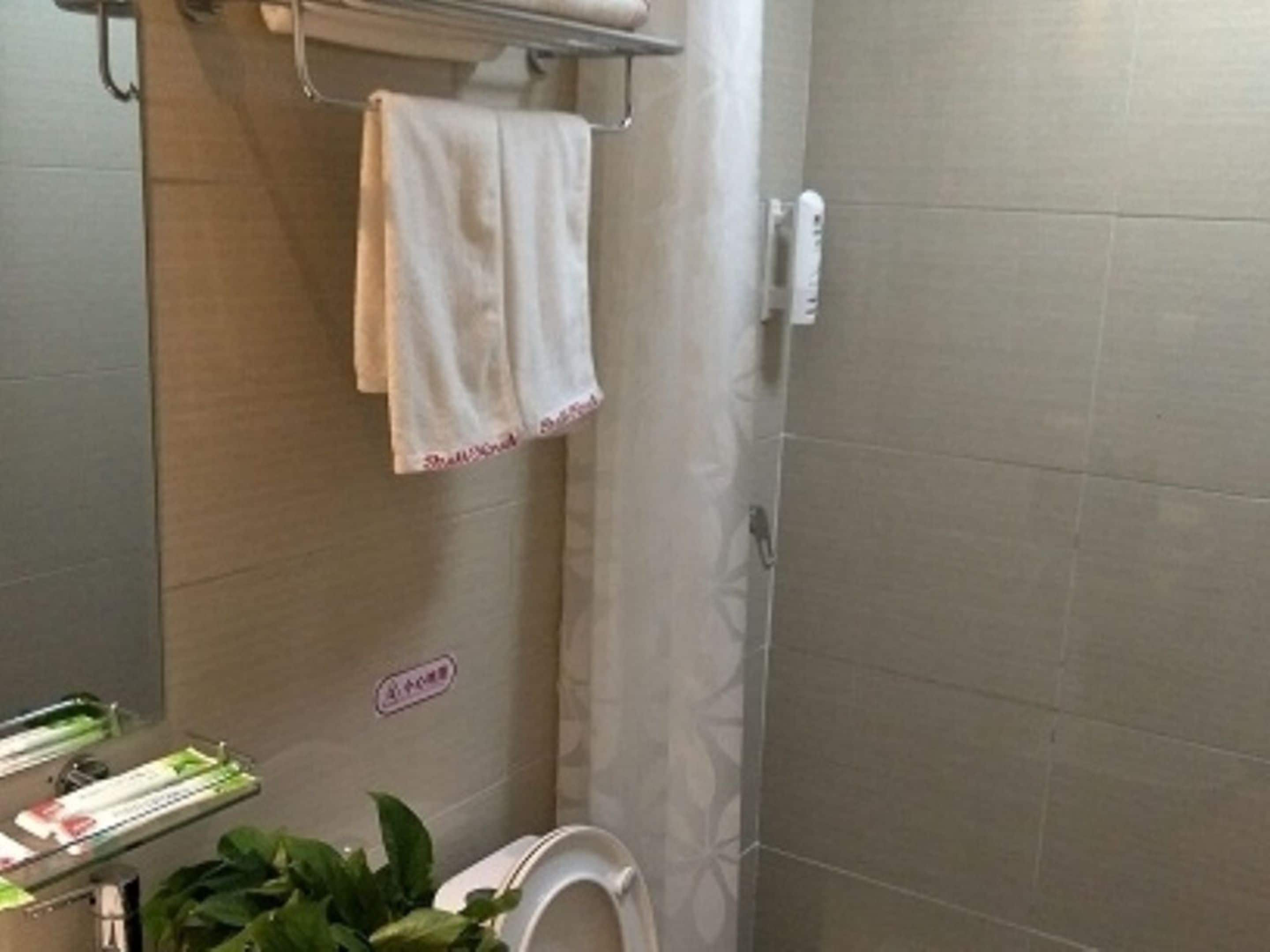 Une salle de bain équipée d’une douche, de toilettes, d’un porte-serviettes avec une serviette et d’une étagère contenant des articles de toilette.