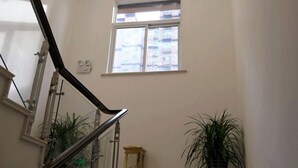 Een trap met een glazen balustrade, een raam met luxaflex en twee potplanten.