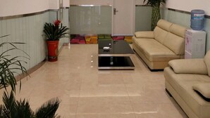 Een moderne lobby met een beige bank, een bijzettafeltje en potplanten.