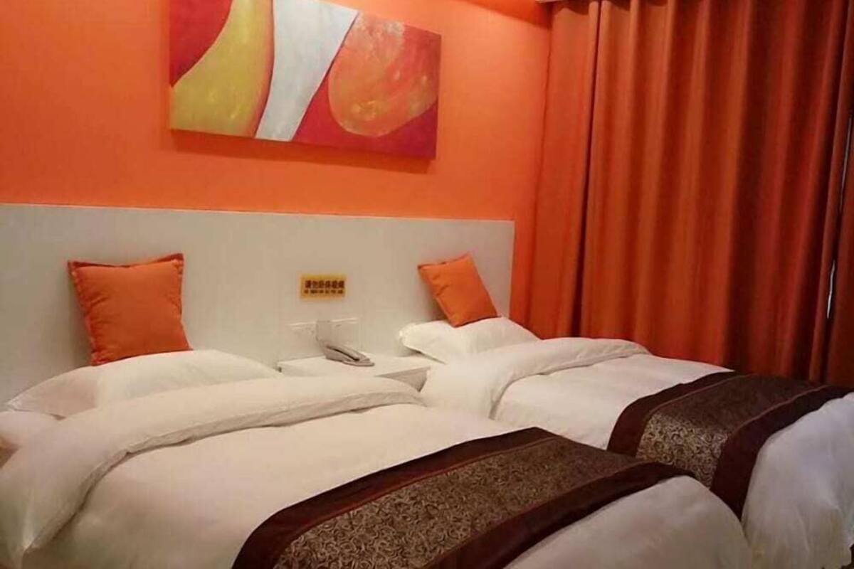 Een hotelkamer met twee bedden, oranje gordijnen en een schilderij aan de wand.