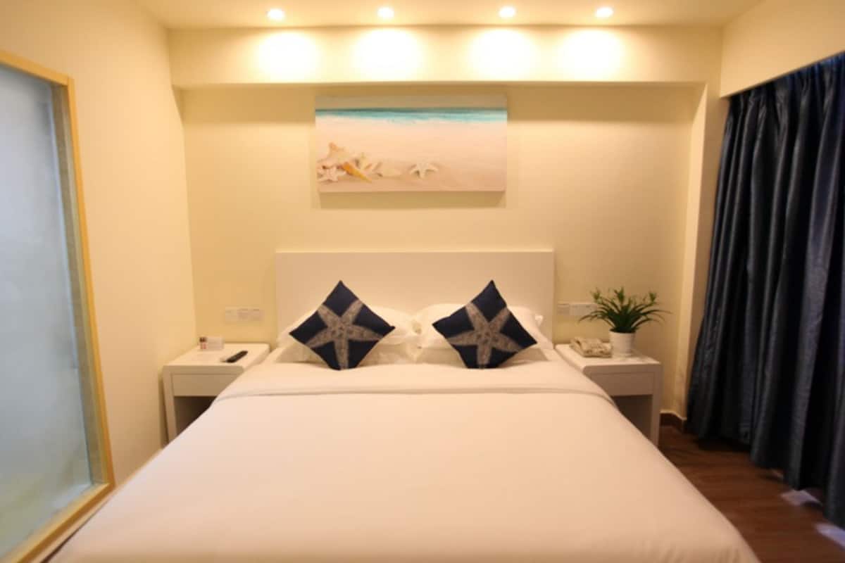 A hotel room with a large bed, two nightstands, a painting above the bed, and a plant on one nightstand.