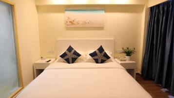 Habitación de hotel con una cama grande, dos mesitas de noche, un cuadro sobre la cama y una planta en una de las mesitas.