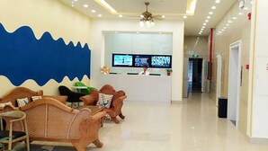 Zona de recepción de un hotel con diseño moderno, que incluye un mostrador de recepción, área de estar con mobiliario de mimbre y una pared azul destacada.