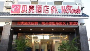 Exterior de un hotel con fachada moderna, amplio acceso de vidrio y plantas en macetas en la entrada.