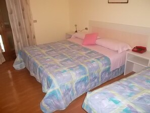 A bedroom with two beds, each with a colorful bedspread, a nightstand with a lamp, and a red alarm clock. - Hotel Residence La Rosa (Castione della Presolana)