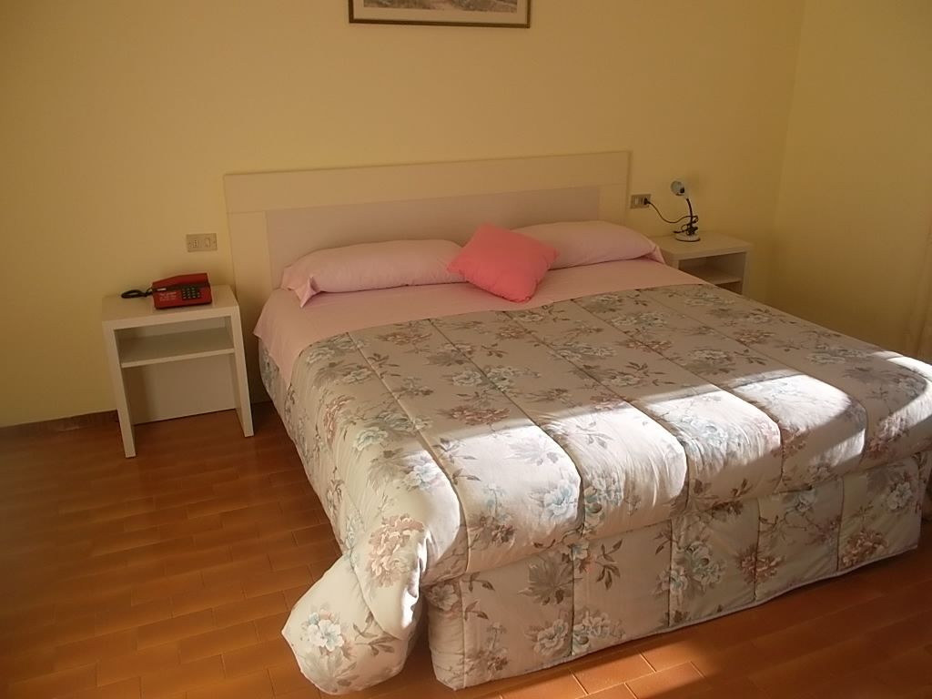 A bedroom with a floral bedspread, a white headboard, a nightstand with a red telephone, and a bedside lamp.