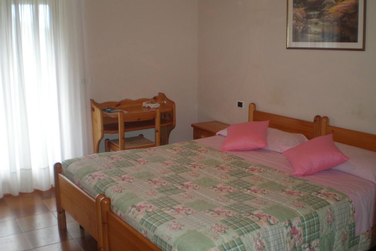 A bedroom with a wooden bed, a wooden nightstand, a wooden chair, and a painting on the wall.