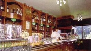A bar with wooden shelves stocked with bottles and a bartender at the counter. - Hotel Residence La Rosa (Castione della Presolana)