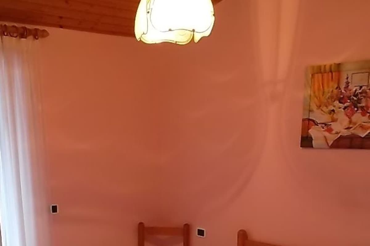Quarto com cama de madeira, colcha estampada, um travesseiro vermelho, uma cadeira de madeira e um quadro na parede.