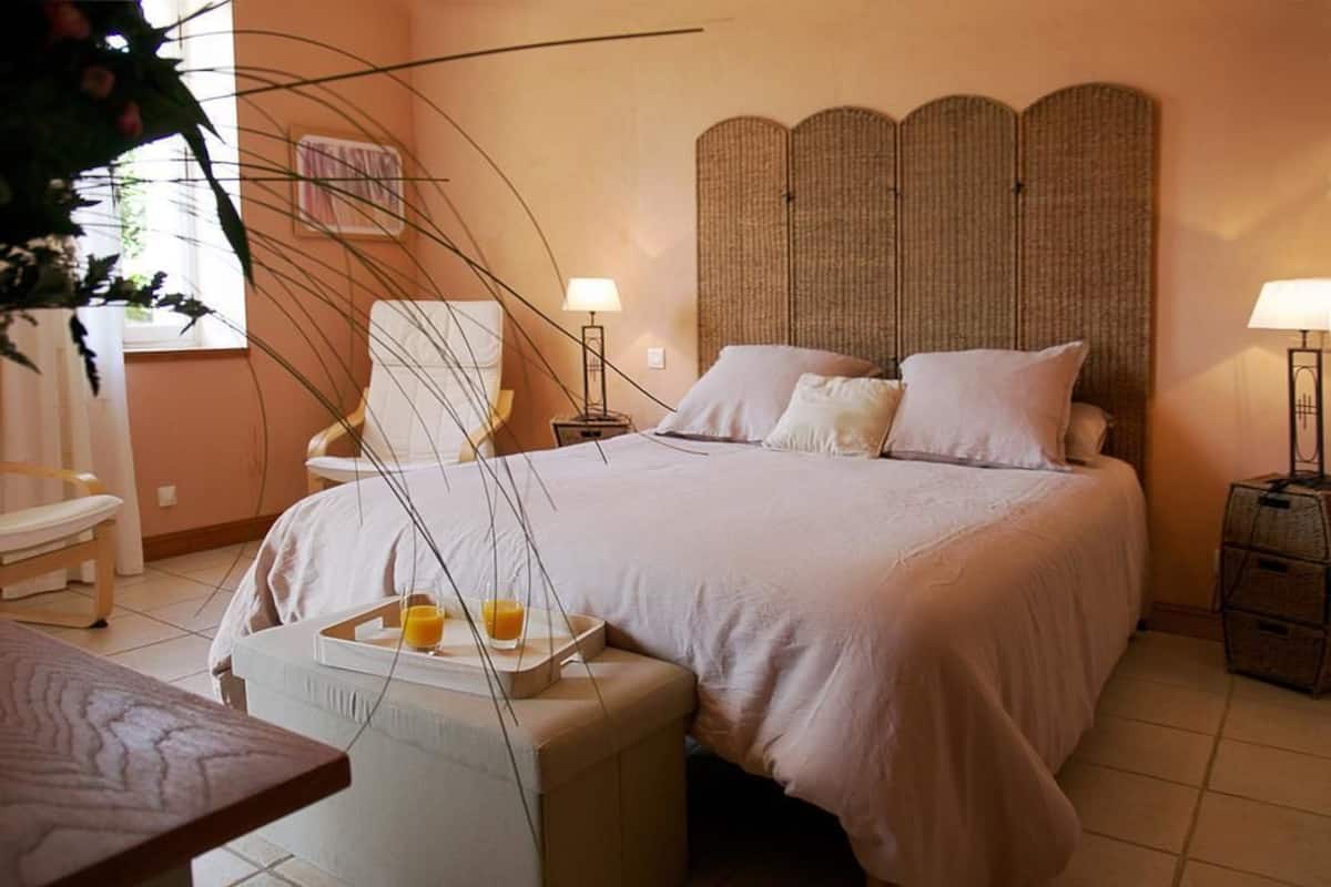 A bedroom with a bed, bedside tables, a chair, a small table with a tray, and a plant.