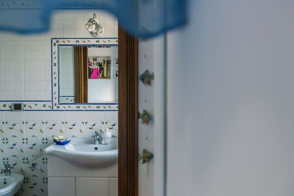 Un baño con lavamanos blanco, un espejo y azulejos estampados con motivos florales.