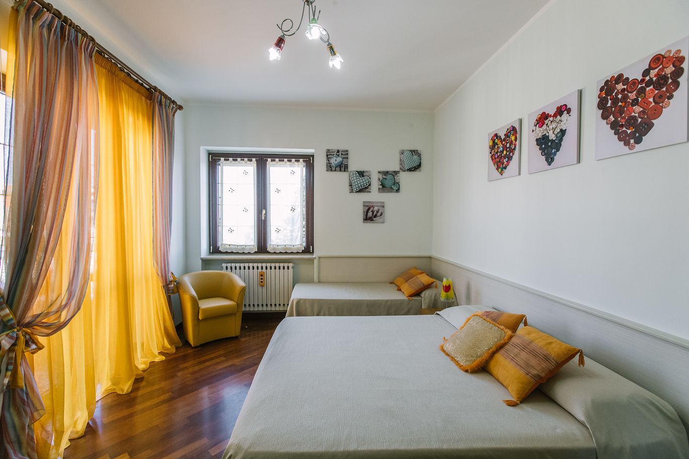 Habitación con dos camas, una silla y un radiador. Hay cortinas, una ventana con persianas y decoración en la pared.