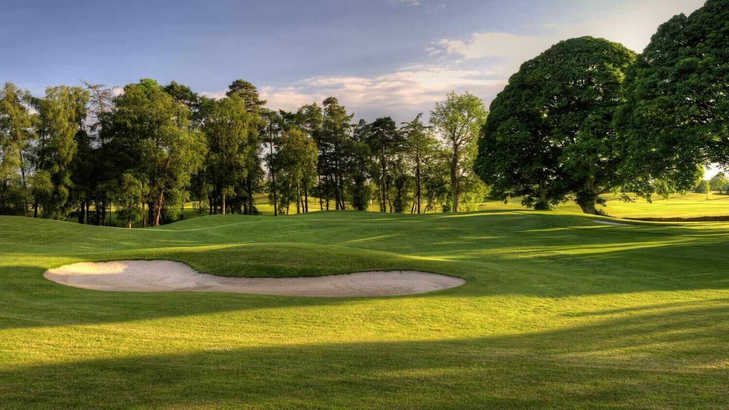 A golf course with a sand bunker, trees, and a clear sky.