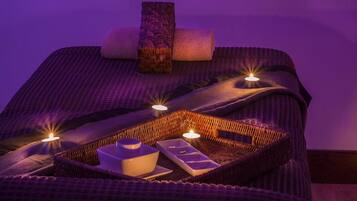 A spa room with a massage table, candles, and a tray with a cup and a small container.