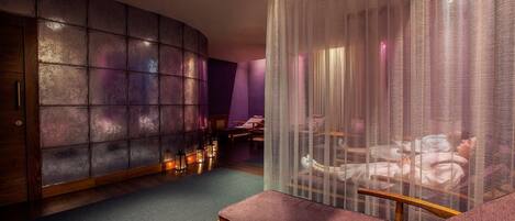 Un cuarto de spa con una camilla de masaje, un banco de madera y una pared con un diseño texturizado.