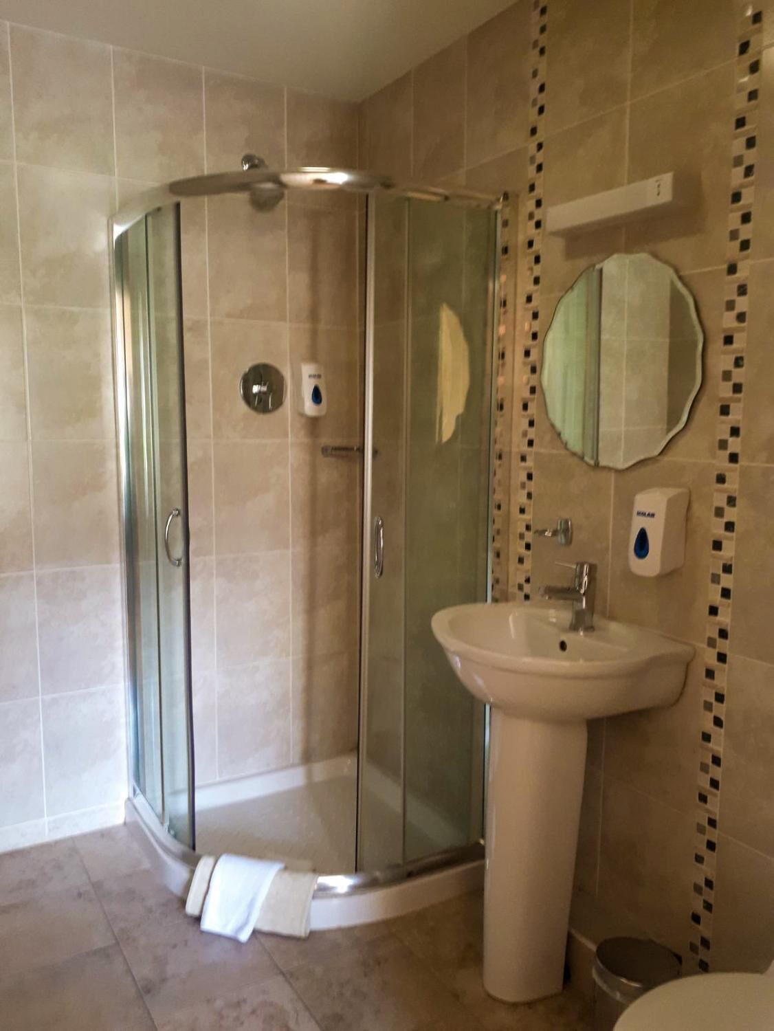 Um banheiro moderno com box de vidro, pia de pedestal e espelho fixado na parede.