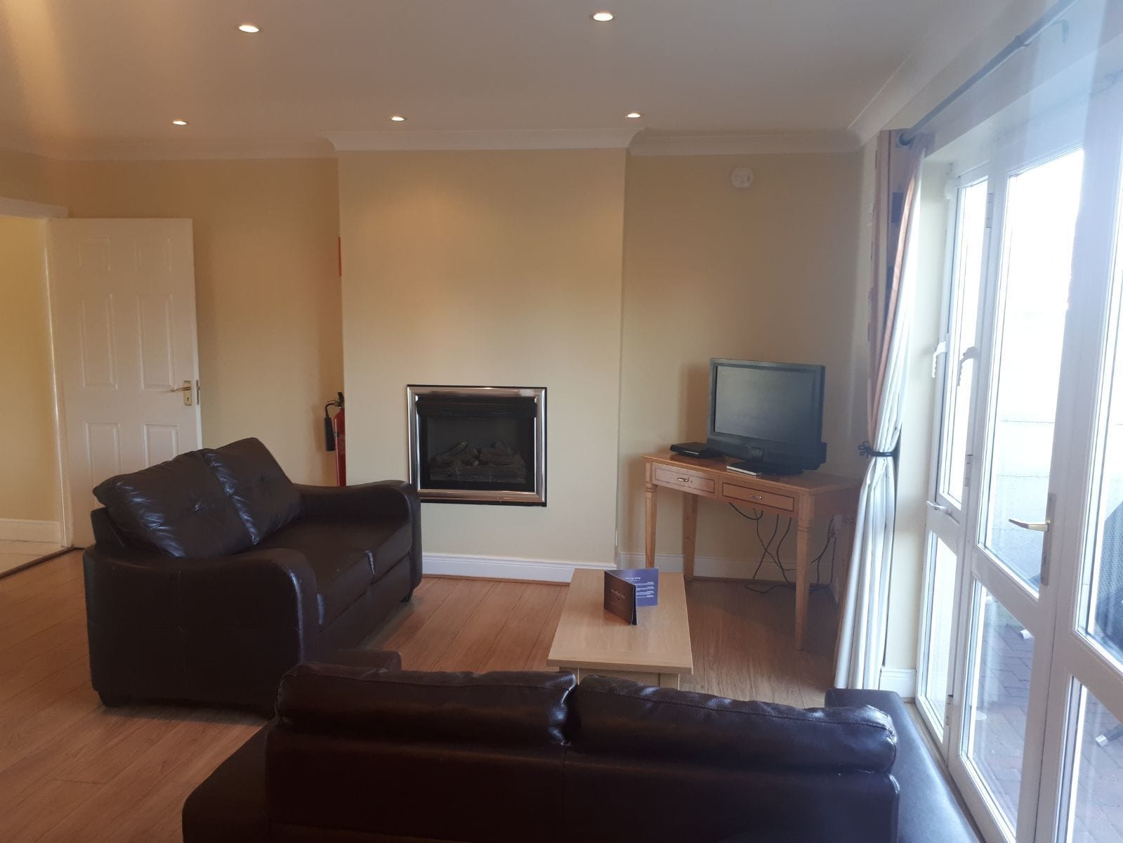A living room with a black leather sofa, a wooden coffee table, a television on a wooden stand, and a fireplace.