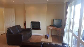 A living room with a black leather sofa, a wooden coffee table, a television on a wooden stand, and a fireplace.