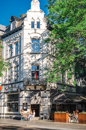A historic building with a balcony, outdoor seating, and a storefront with a sign. - Alex Maastricht (Maastricht)