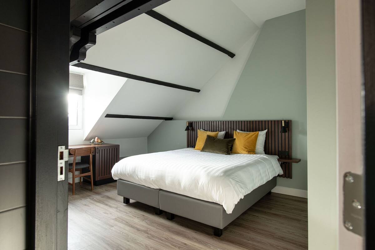 A bedroom with a sloped ceiling, a bed with a wooden headboard, and a desk with a chair.