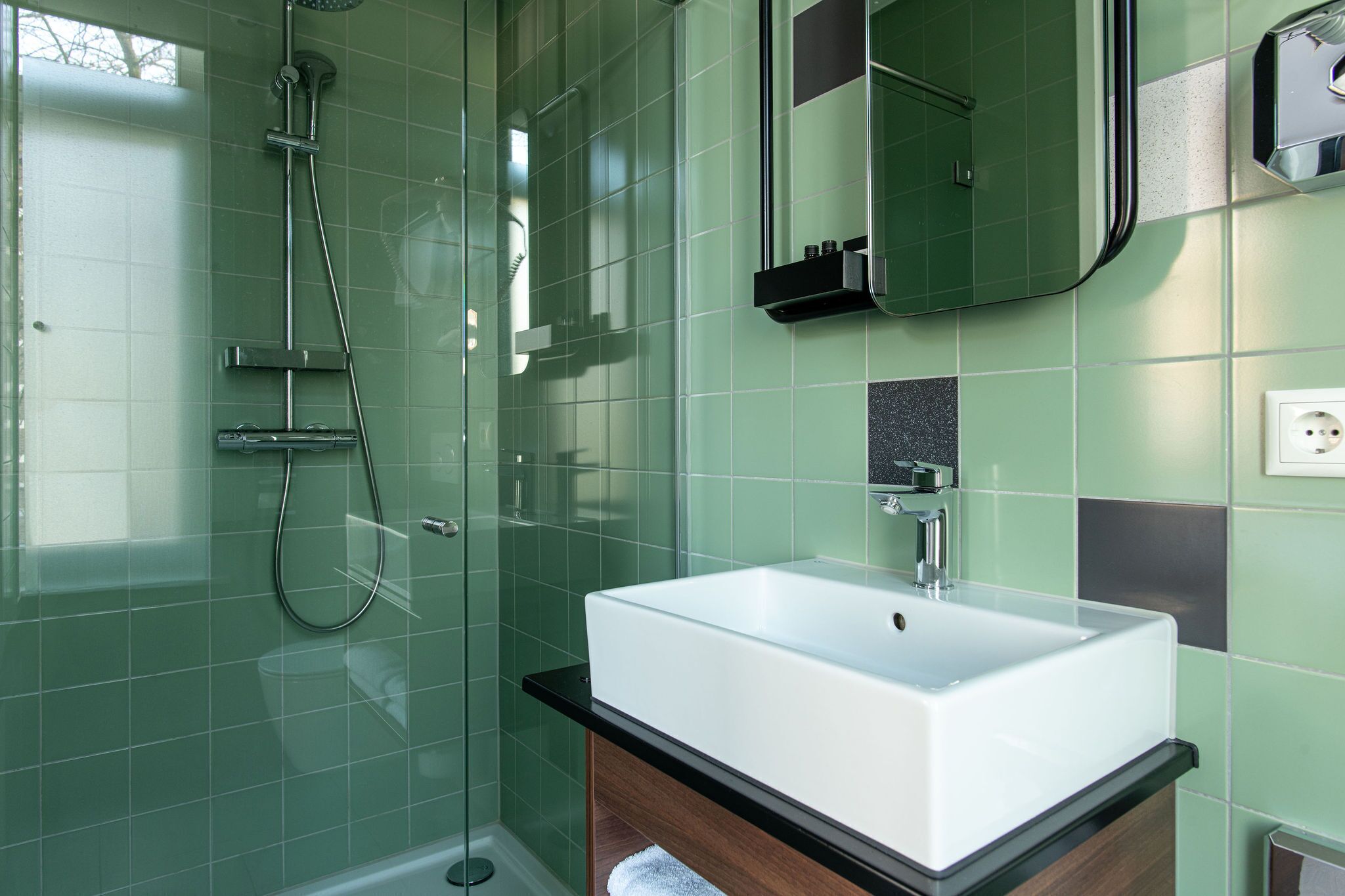Une salle de bain avec une douche à parois de verre, un lavabo blanc et un miroir au-dessus.