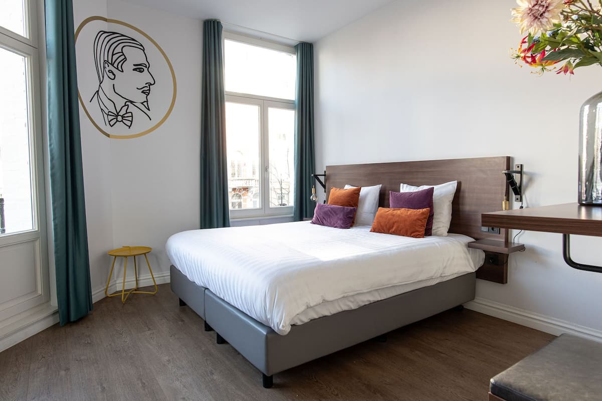 A modern bedroom with a large bed, a bedside table, a small stool, and a wall-mounted shelf.