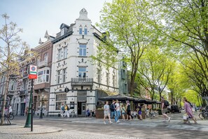 A historic building with a corner entrance, a cafe with outdoor seating, and a tree-lined street. - Alex Maastricht (Maastricht)