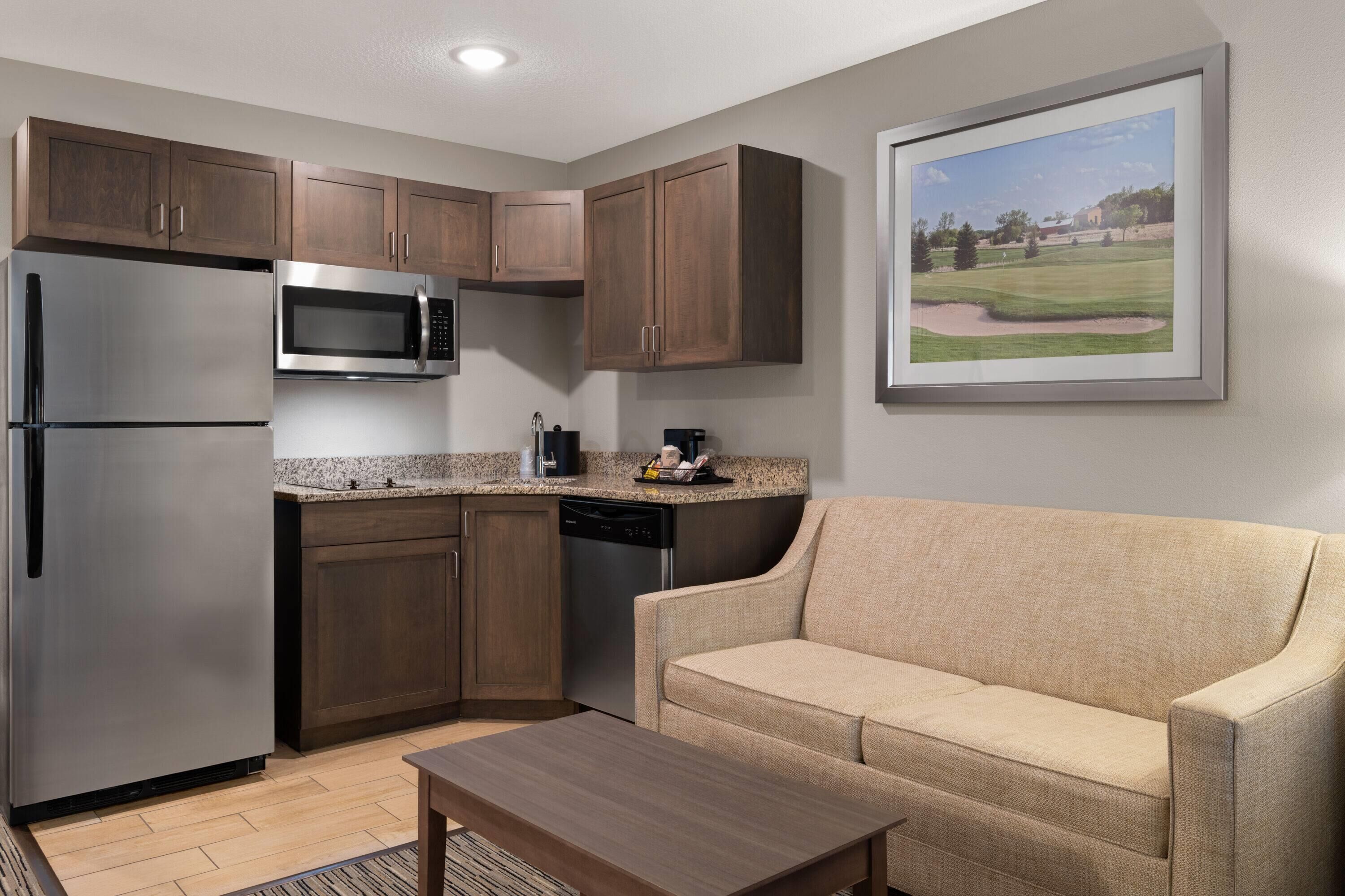 A compact kitchen with built-in appliances, a wooden cabinet, and a beige sofa.