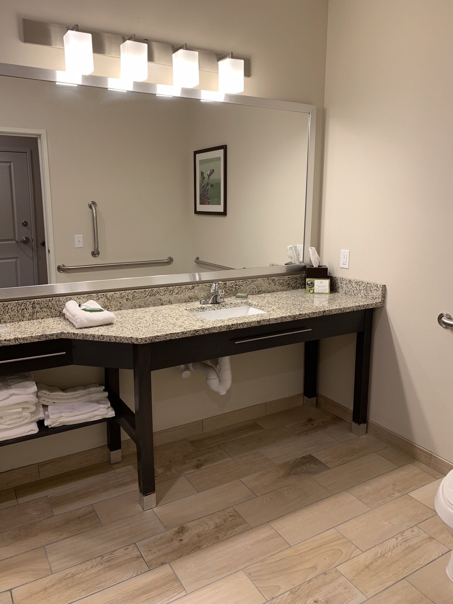 A bathroom with a granite countertop, a large mirror, a towel rack, and a hand dryer.
