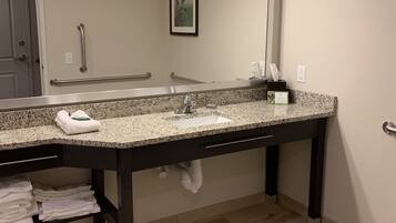 A bathroom with a granite countertop, a large mirror, a towel rack, and a hand dryer.