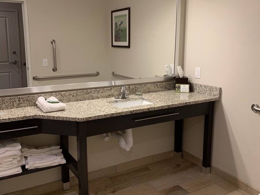 A bathroom with a granite countertop, a large mirror, a towel rack, and a hand dryer.
