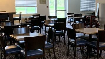 A dining area with multiple tables and chairs, a carpeted floor, and windows with blinds.