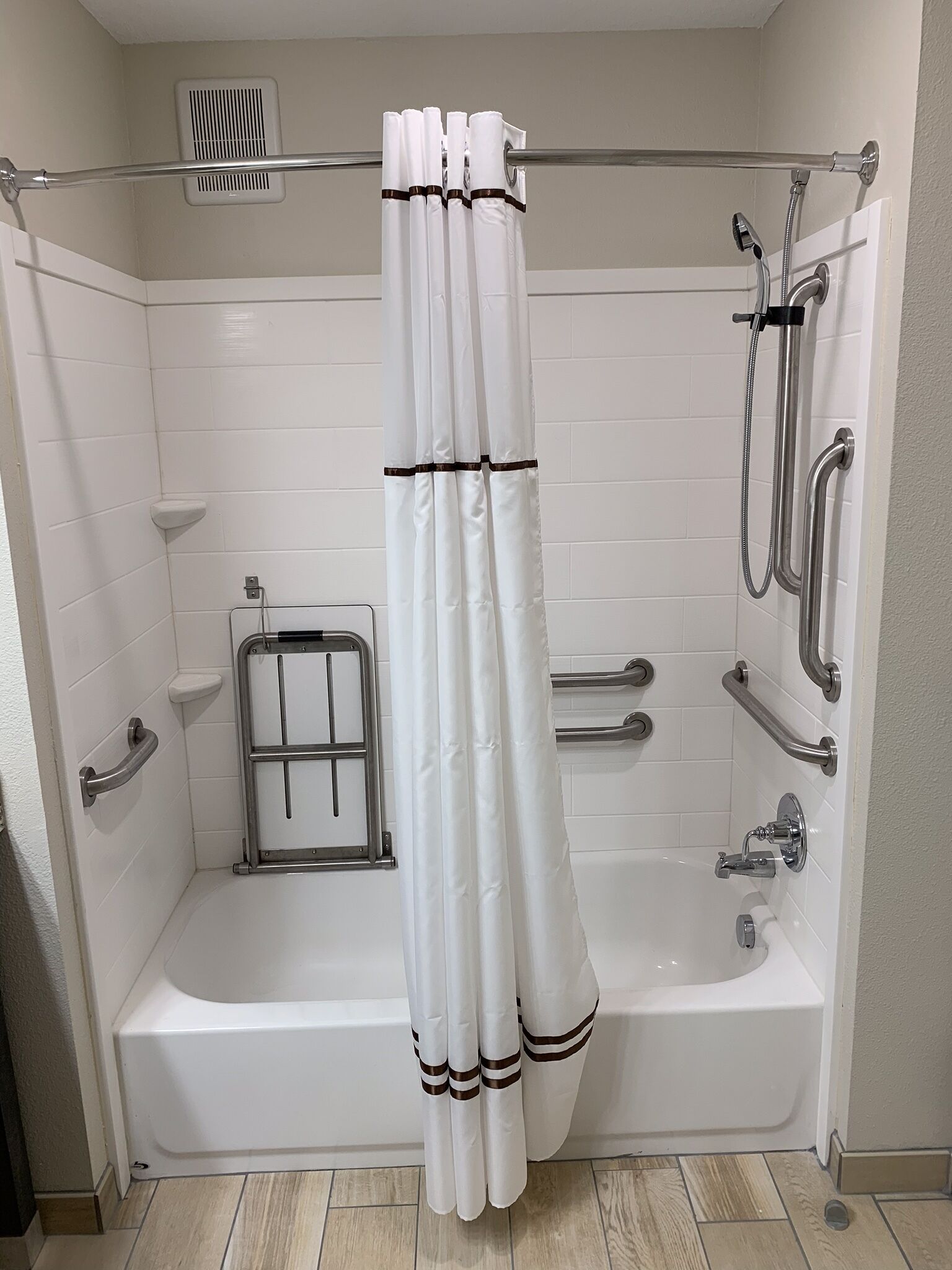 A modern bathroom with a bathtub, shower, and handrails.