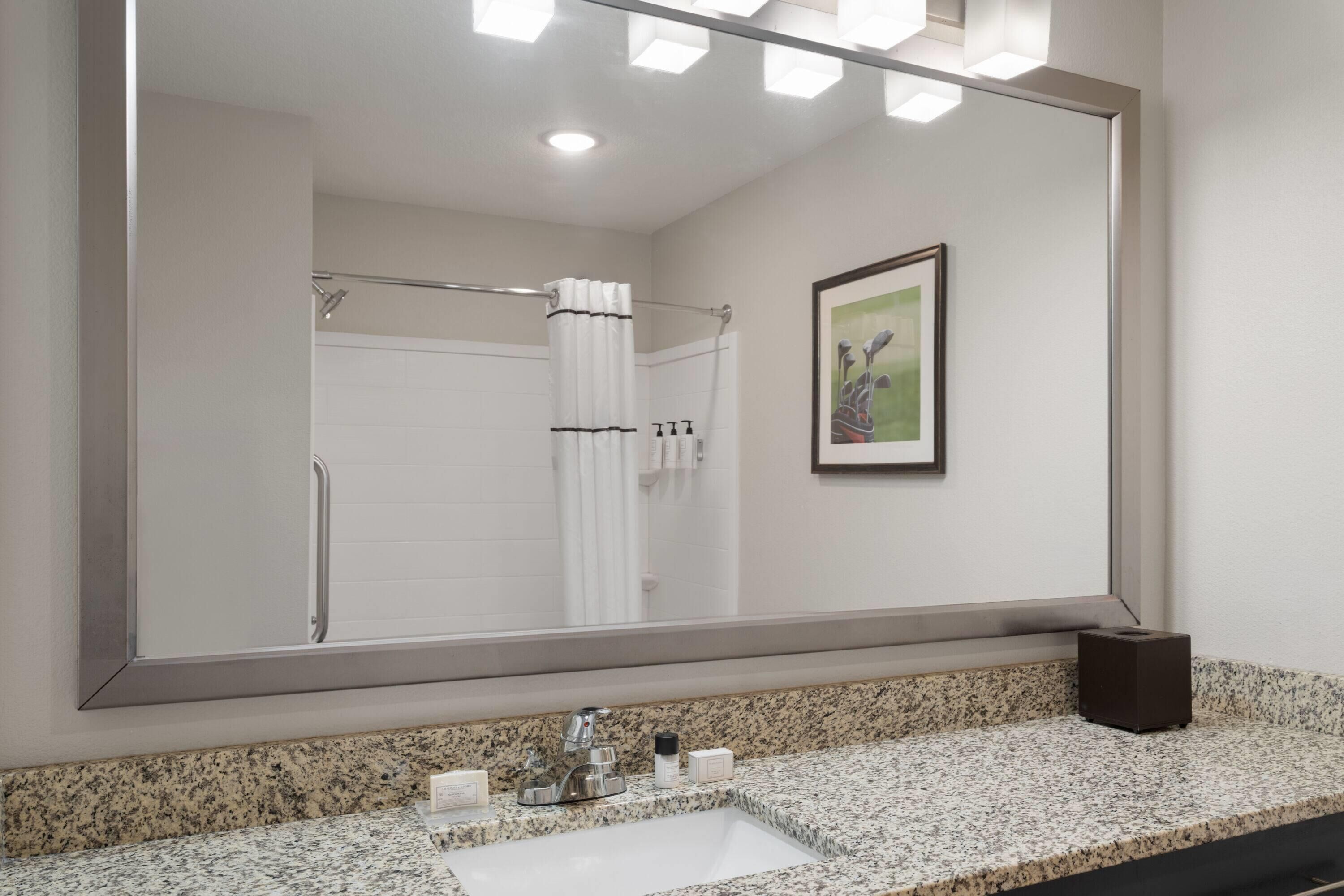 A bathroom with a large mirror, a granite countertop, a sink, and a shower with a curtain.