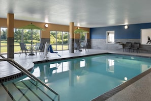 Una piscina interior con paredes de vidrio transparente, múltiples sillones de descanso y sombrillas.