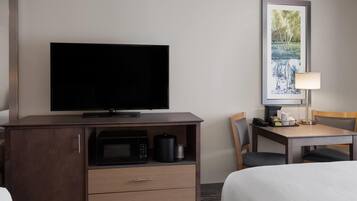 A hotel room with a flat-screen TV on a wooden cabinet, a microwave, a coffee maker, and a dining table with chairs.