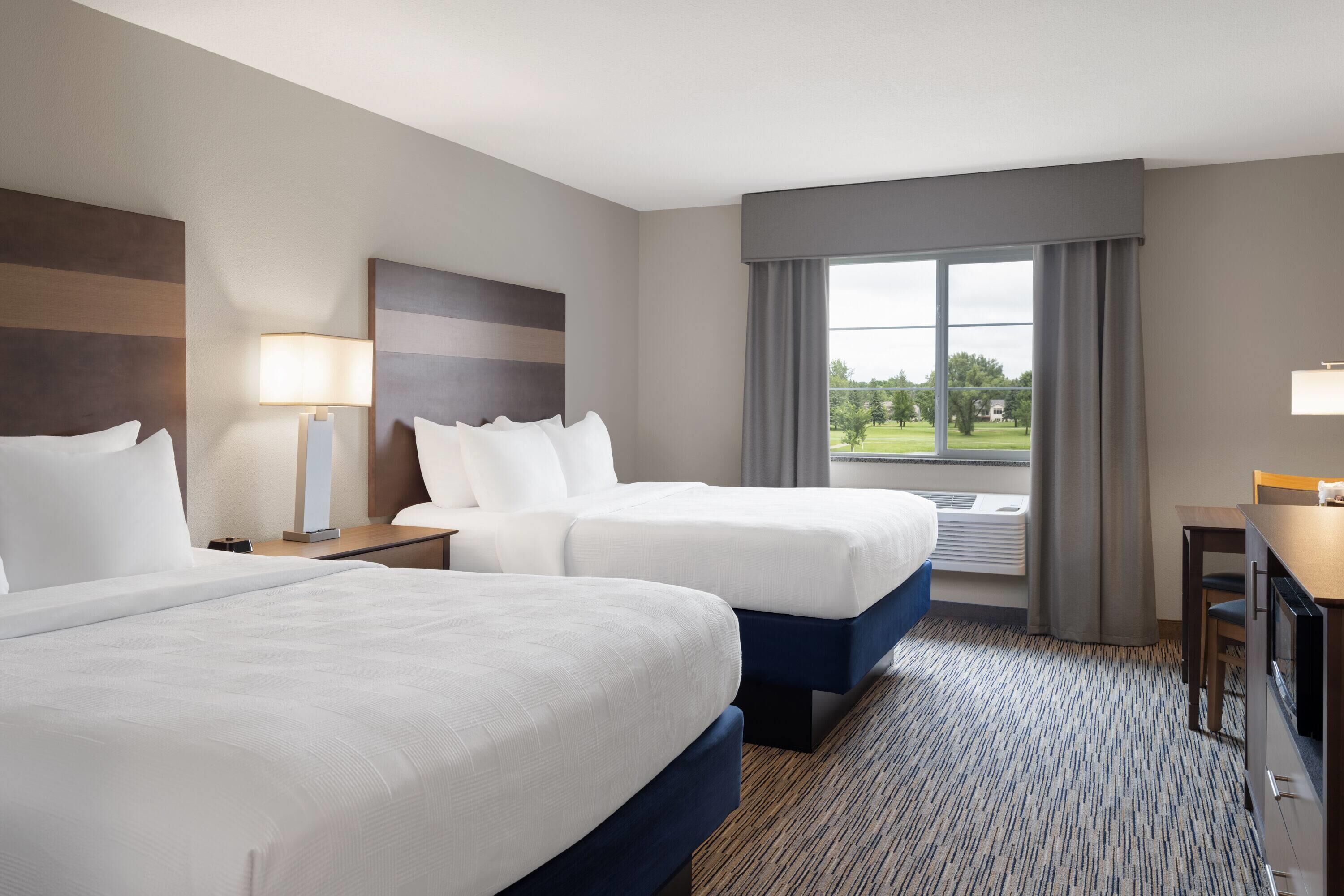 A hotel room with two beds, a desk, and a view of a park.