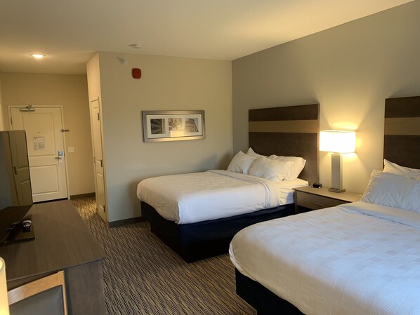 Ein Hotelzimmer mit zwei Betten, einem Schreibtisch, einer Lampe und einem gerahmten Bild an der Wand.