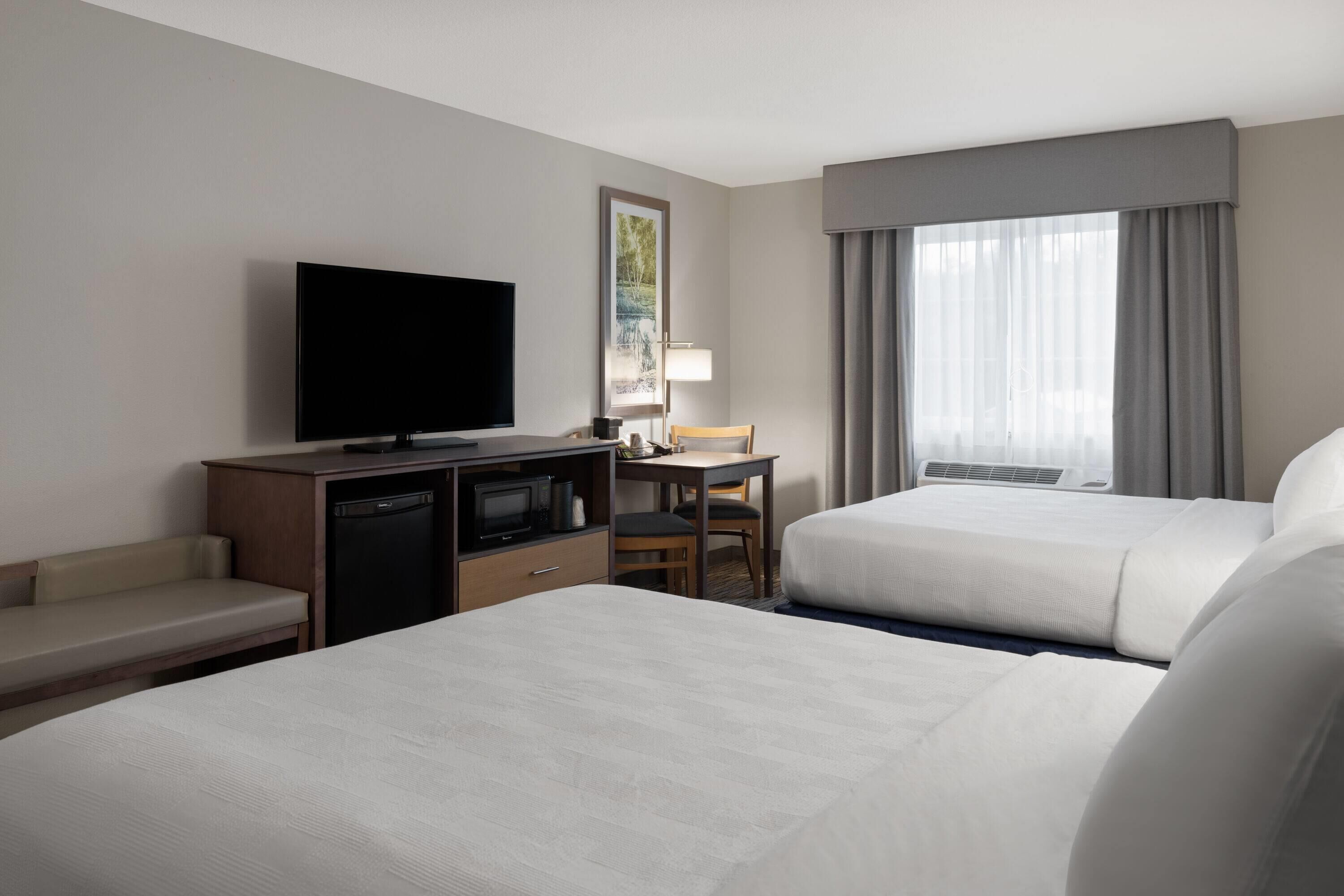 Habitación de hotel con dos camas, un escritorio con silla, televisor y ventana con cortinas.