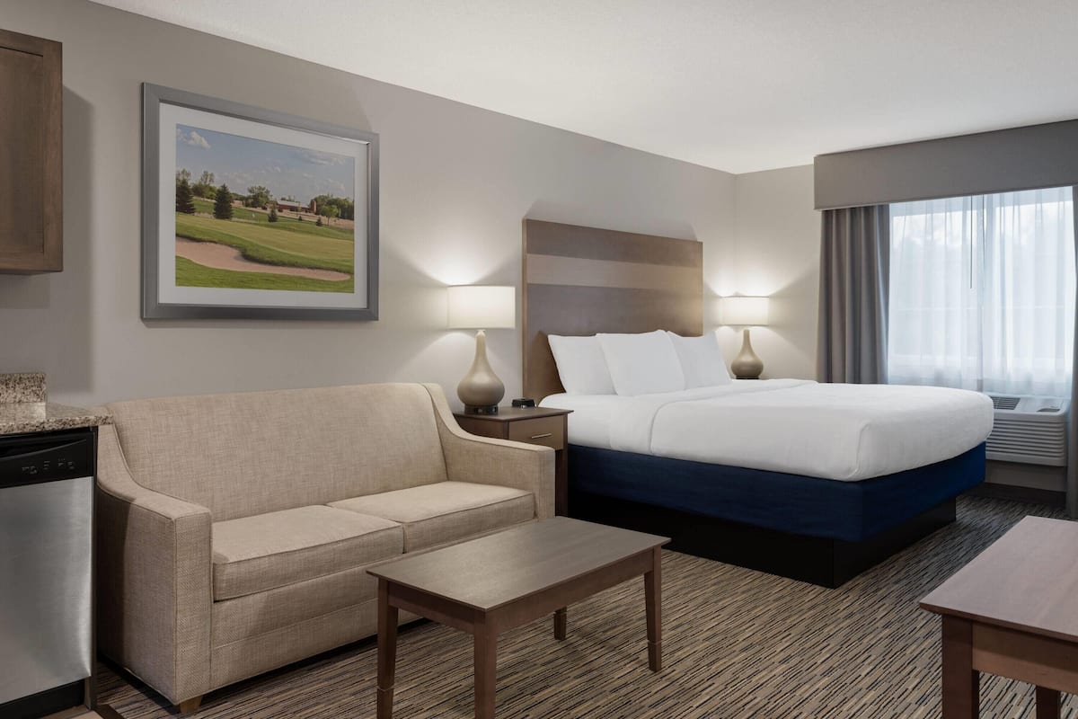 Una habitación de hotel con una cama, un sofá, una mesita, una lámpara y un cuadro en la pared.