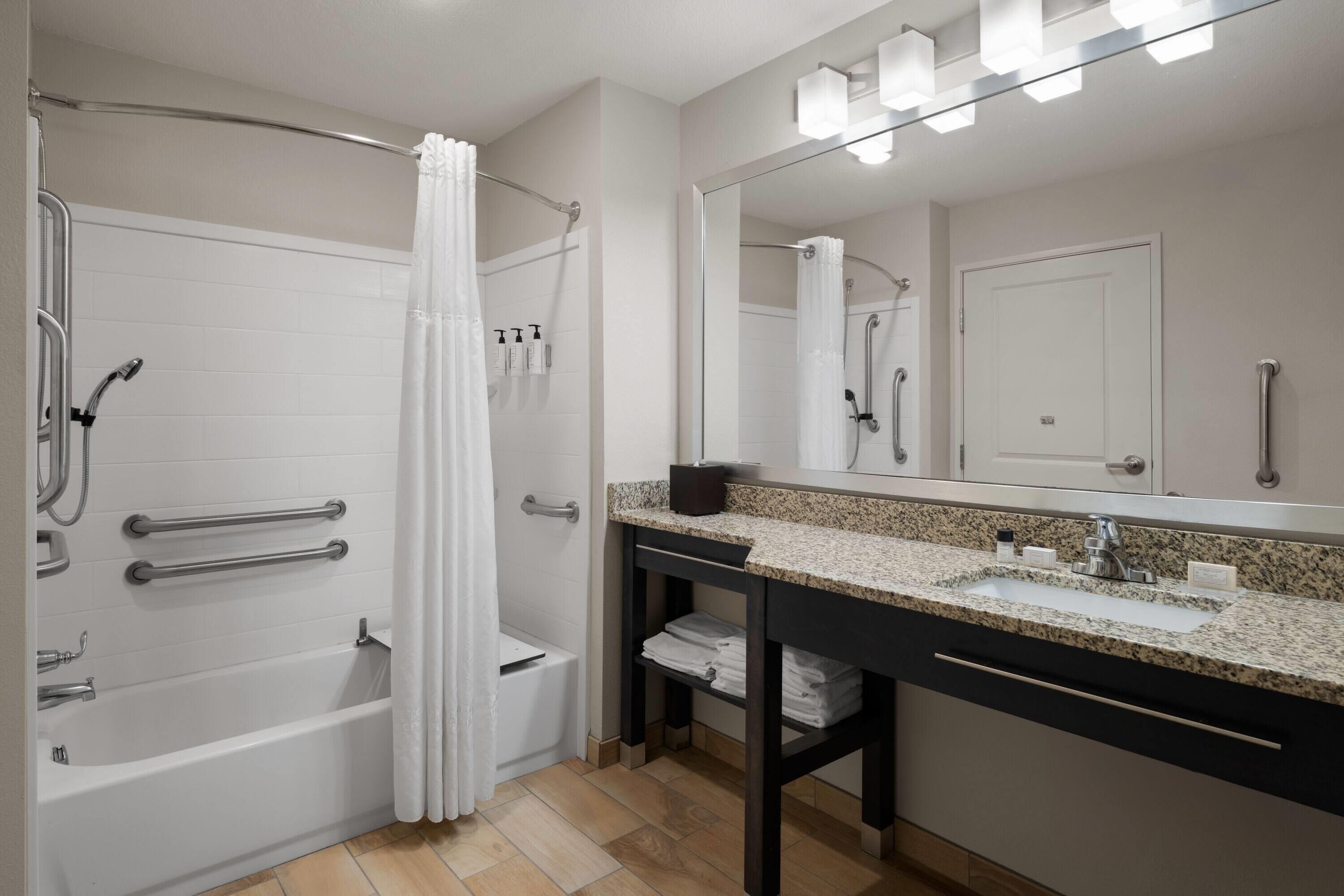 A modern bathroom with a walk-in shower, grab bars, a vanity with a sink, and a large mirror.