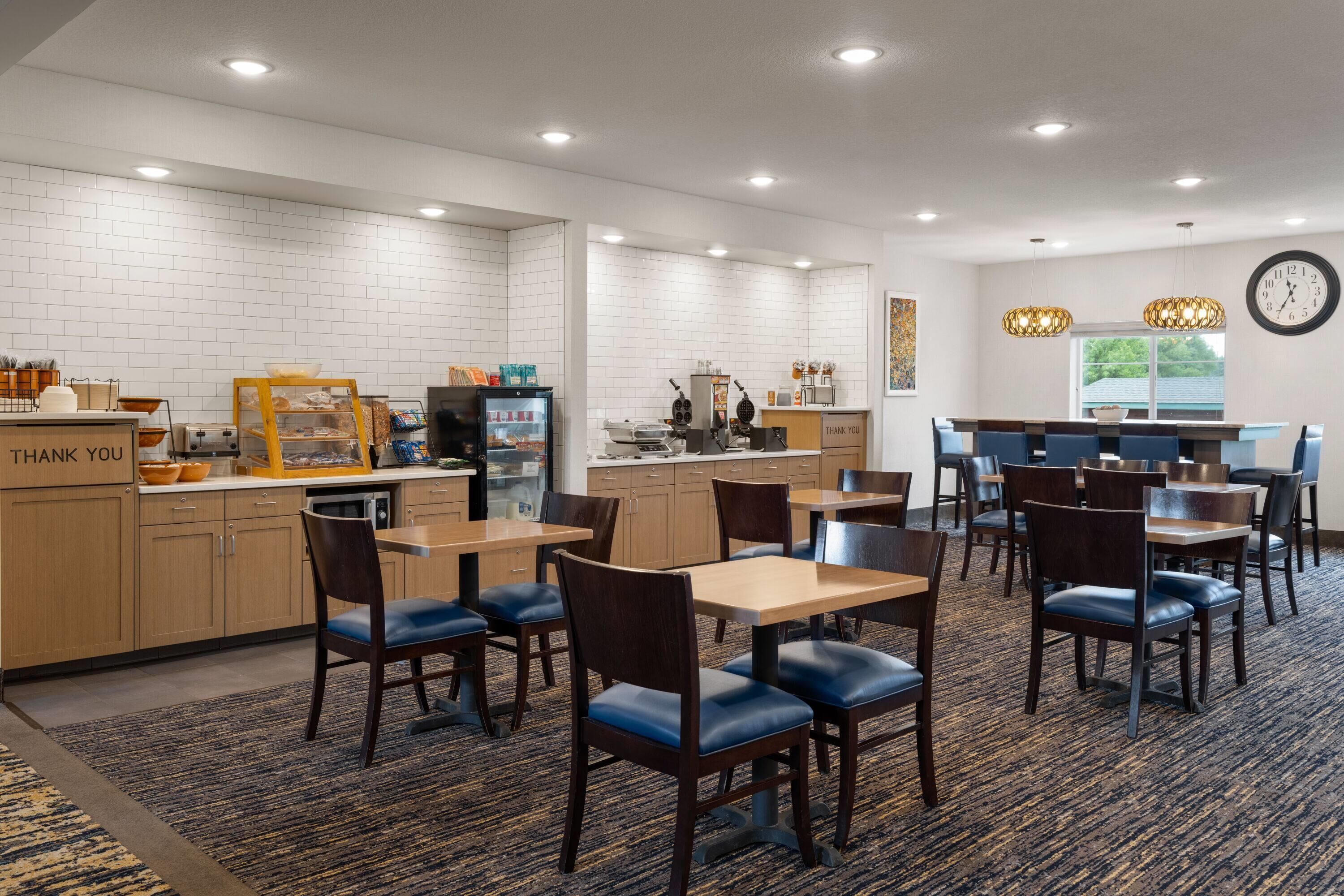 A hotel lobby with a reception desk, seating area, and kitchen in the background.