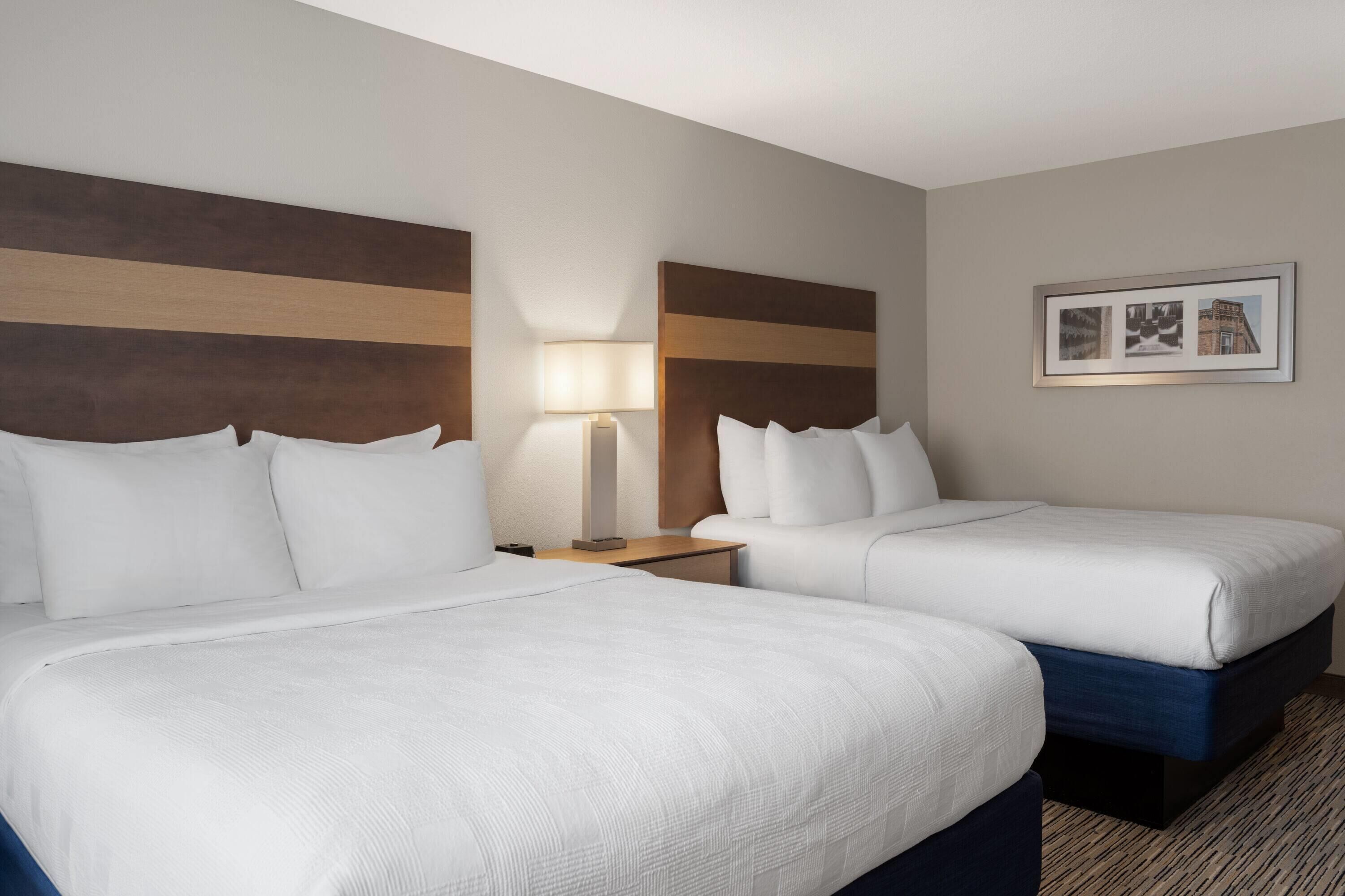 A hotel room with two beds, a nightstand with a lamp, and a framed picture on the wall.