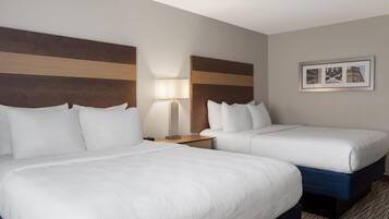 A hotel room with two beds, a nightstand with a lamp, and a framed picture on the wall.