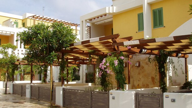 Un patio con pérgola, plantas en macetas y una entrada con reja.